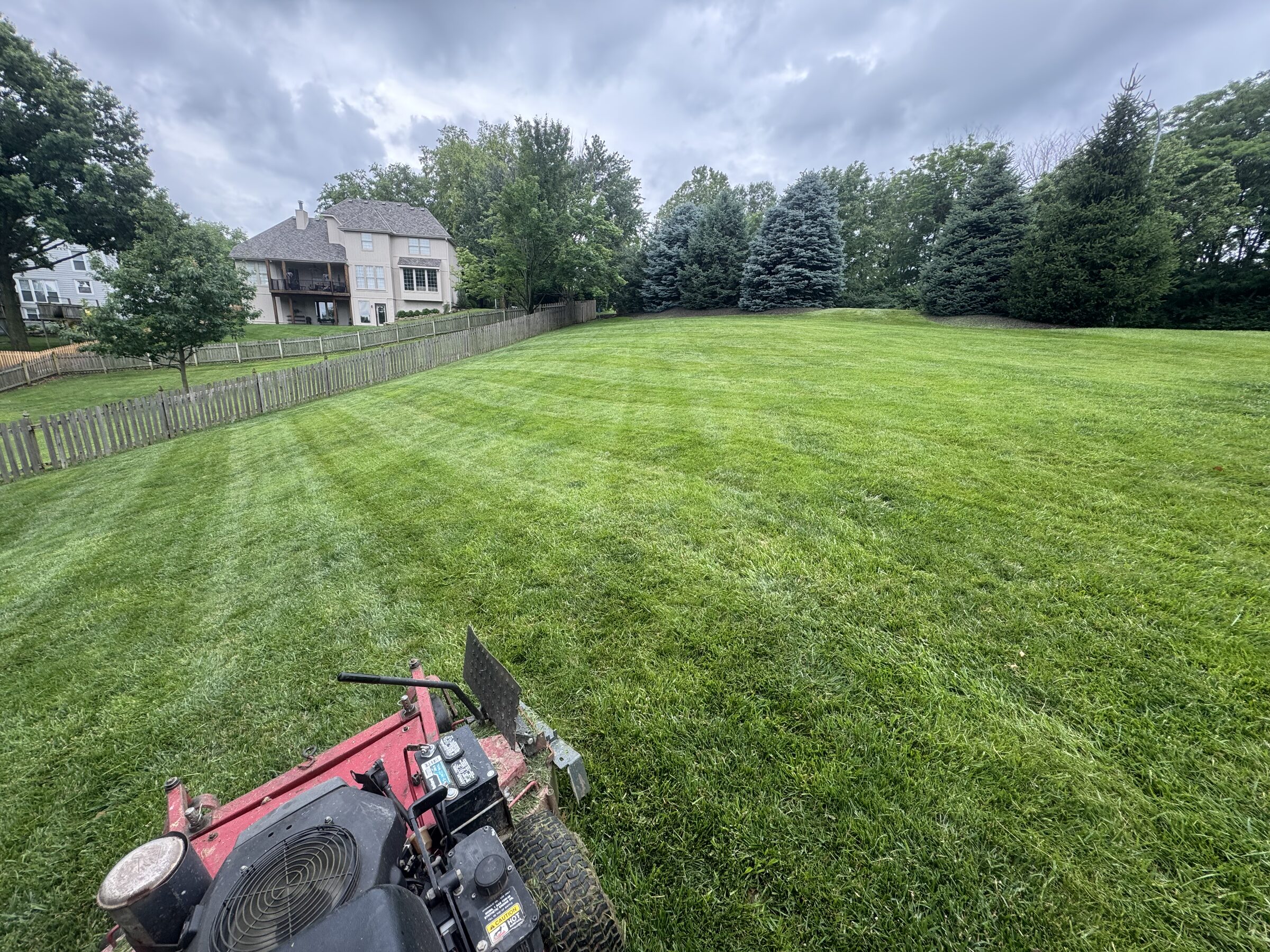 View from a stand-on mower cutting stripes across a large backyard